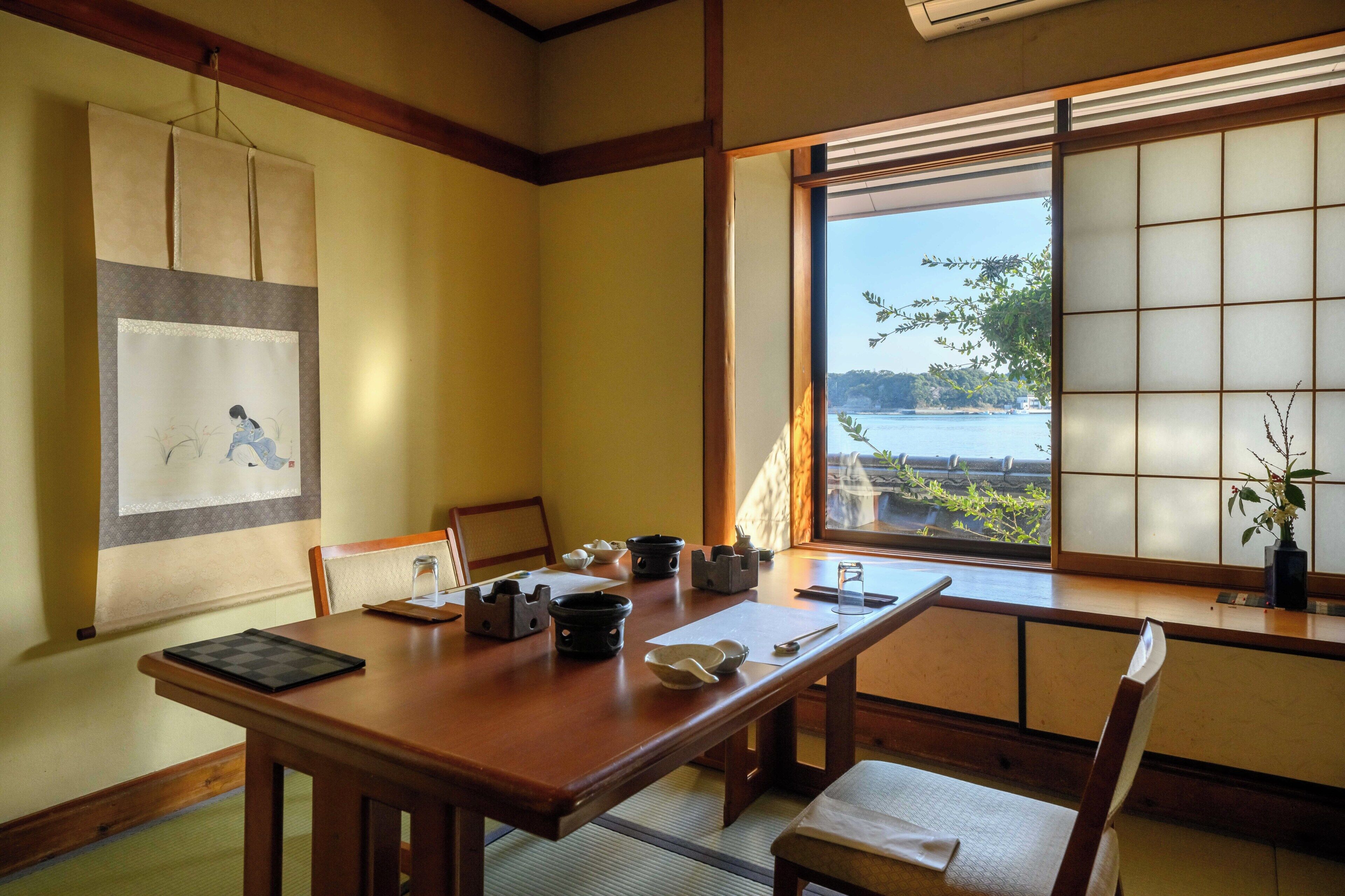 A traditional Japanese room with tatami flooring, a low table with tea utensils, a shoji screen, and a view of a body of water.