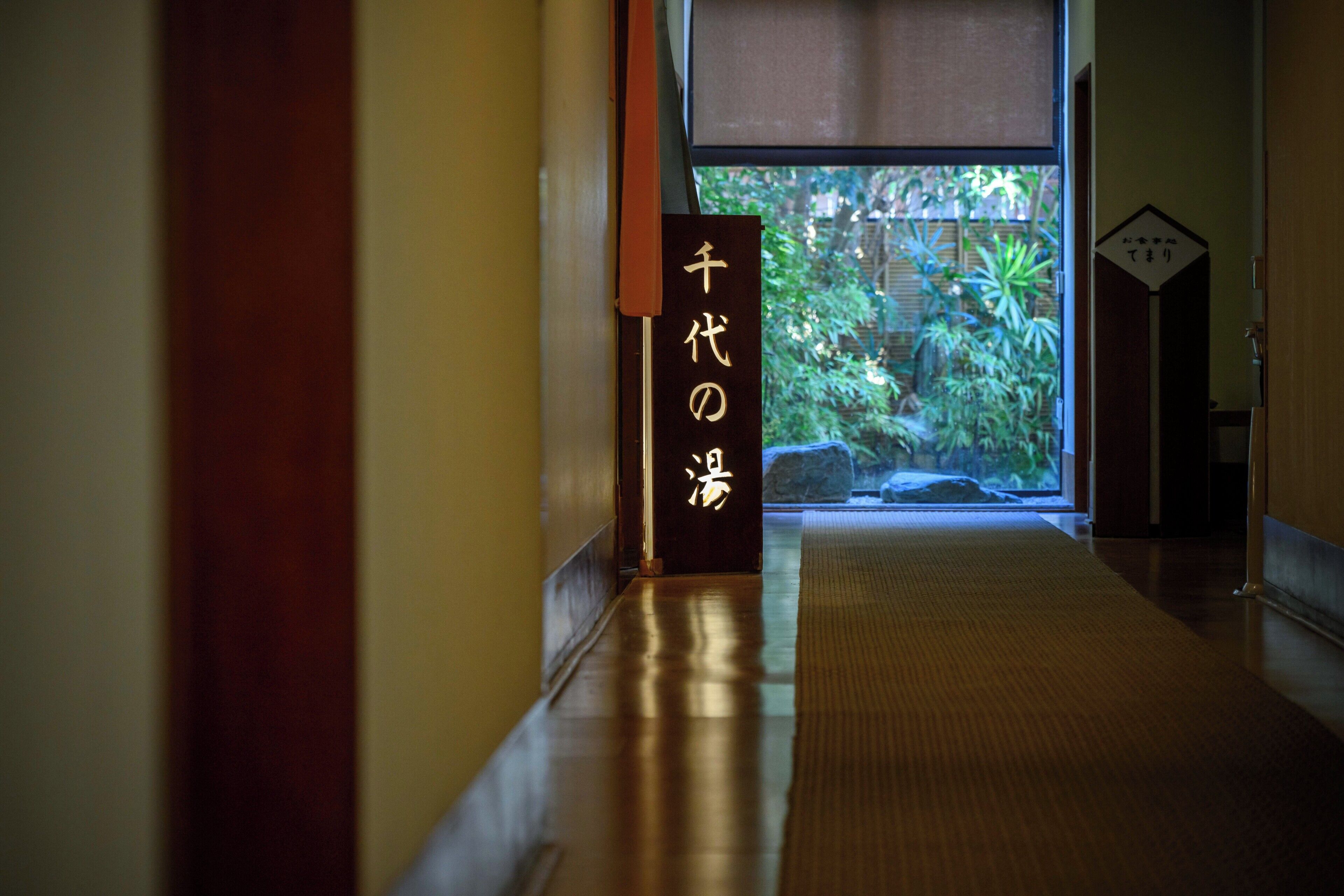 A hallway with a wooden floor, a tatami mat, and a sign with Japanese characters.