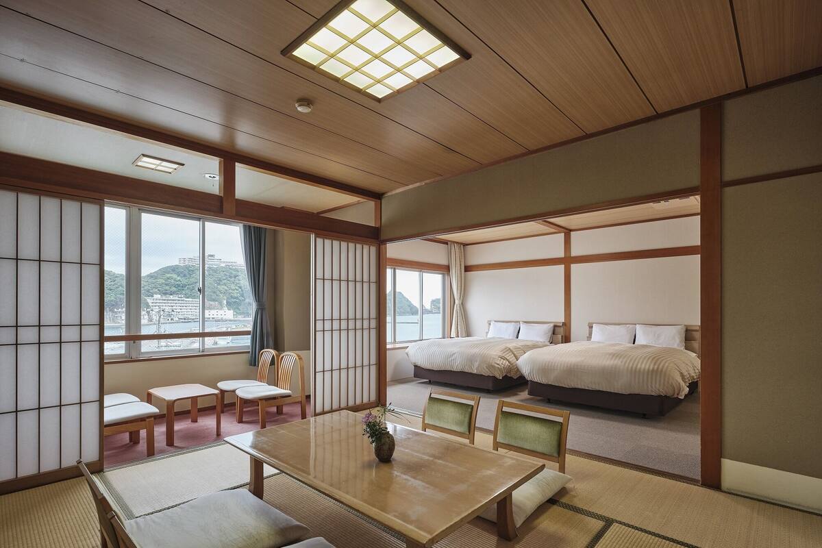 A traditional Japanese-style room with tatami flooring, a low wooden table, and two beds with white bedding.