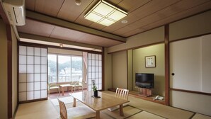 Una tradizionale stanza giapponese con pavimento in tatami, un tavolino con cuscini, una TV e una porta scorrevole.