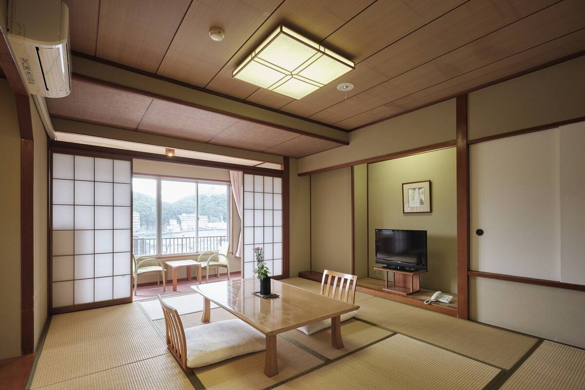 A traditional Japanese room with tatami flooring, a low table with cushions, a TV, and a sliding door.