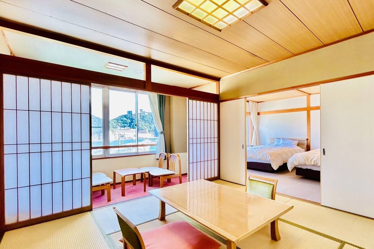 A traditional Japanese room with tatami flooring, a low table, and a bed with a futon.
