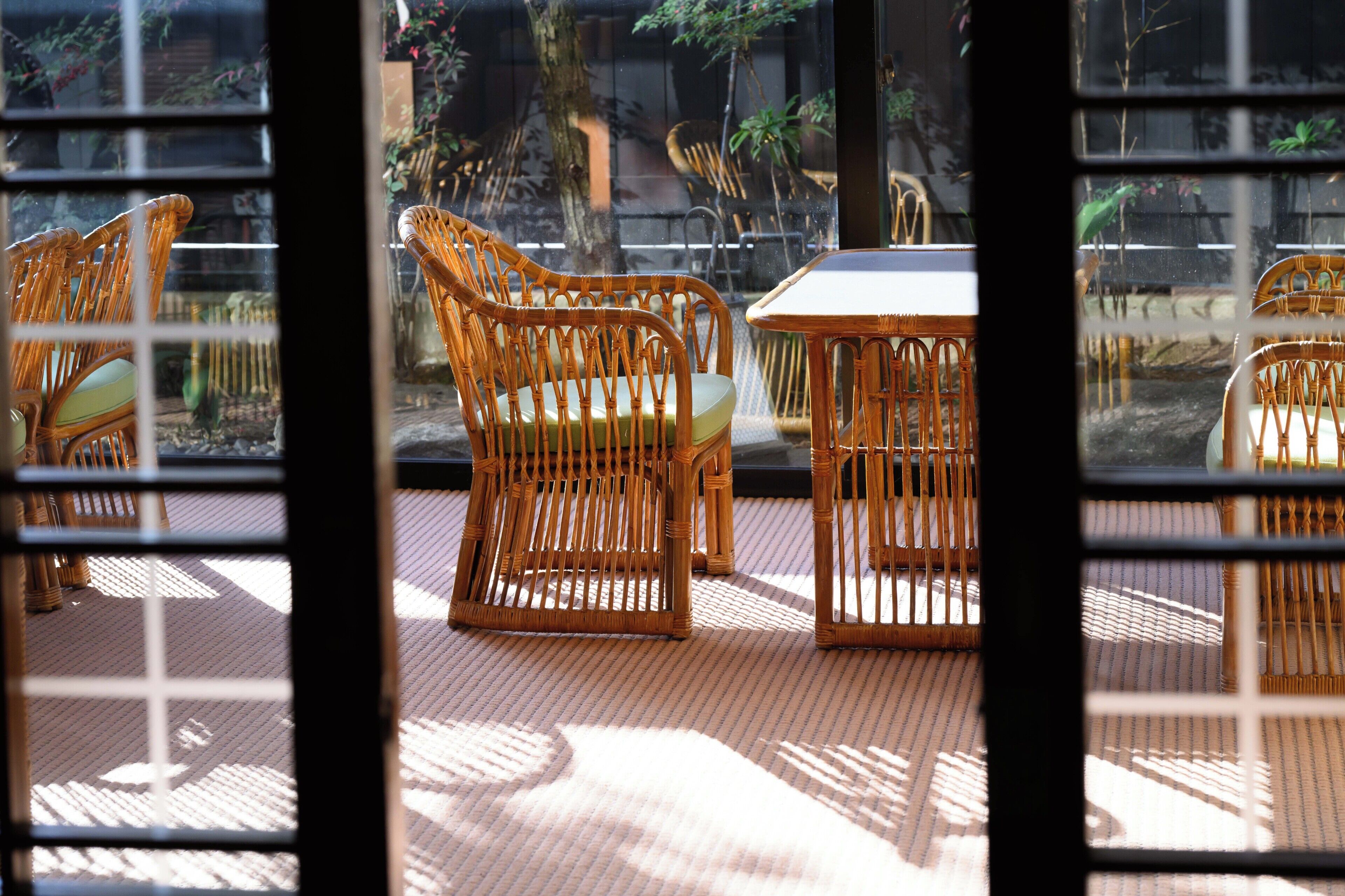 A room with wicker furniture, including chairs and a table, through a window with a grid pattern.