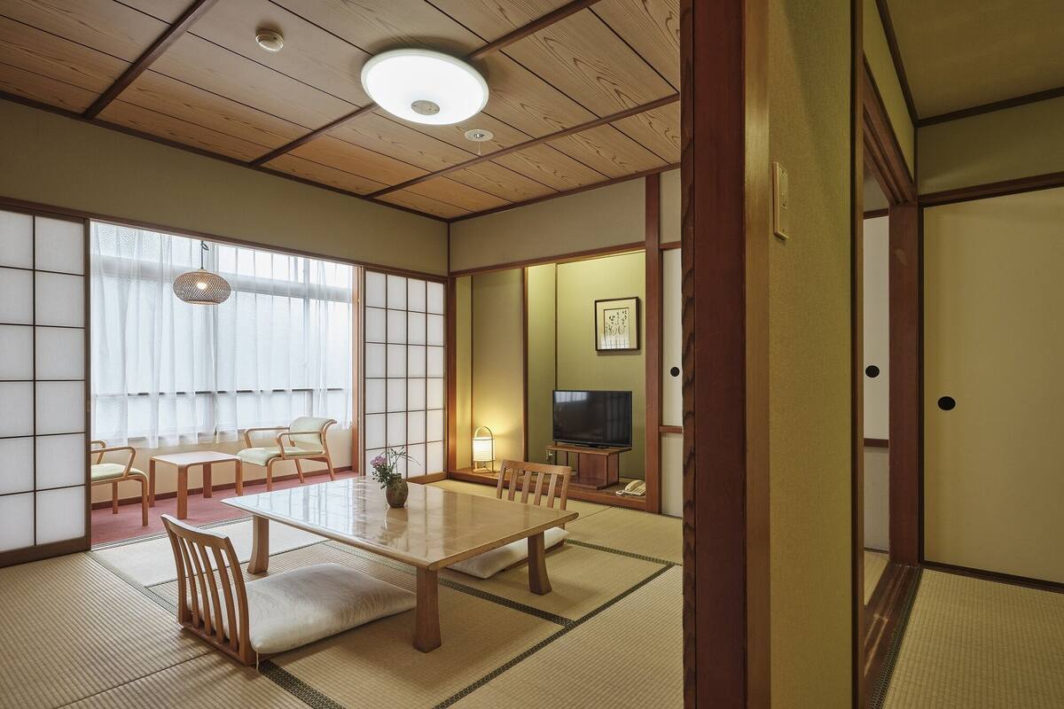 A traditional Japanese room with tatami flooring, a low table, chairs, a television, and sliding doors.
