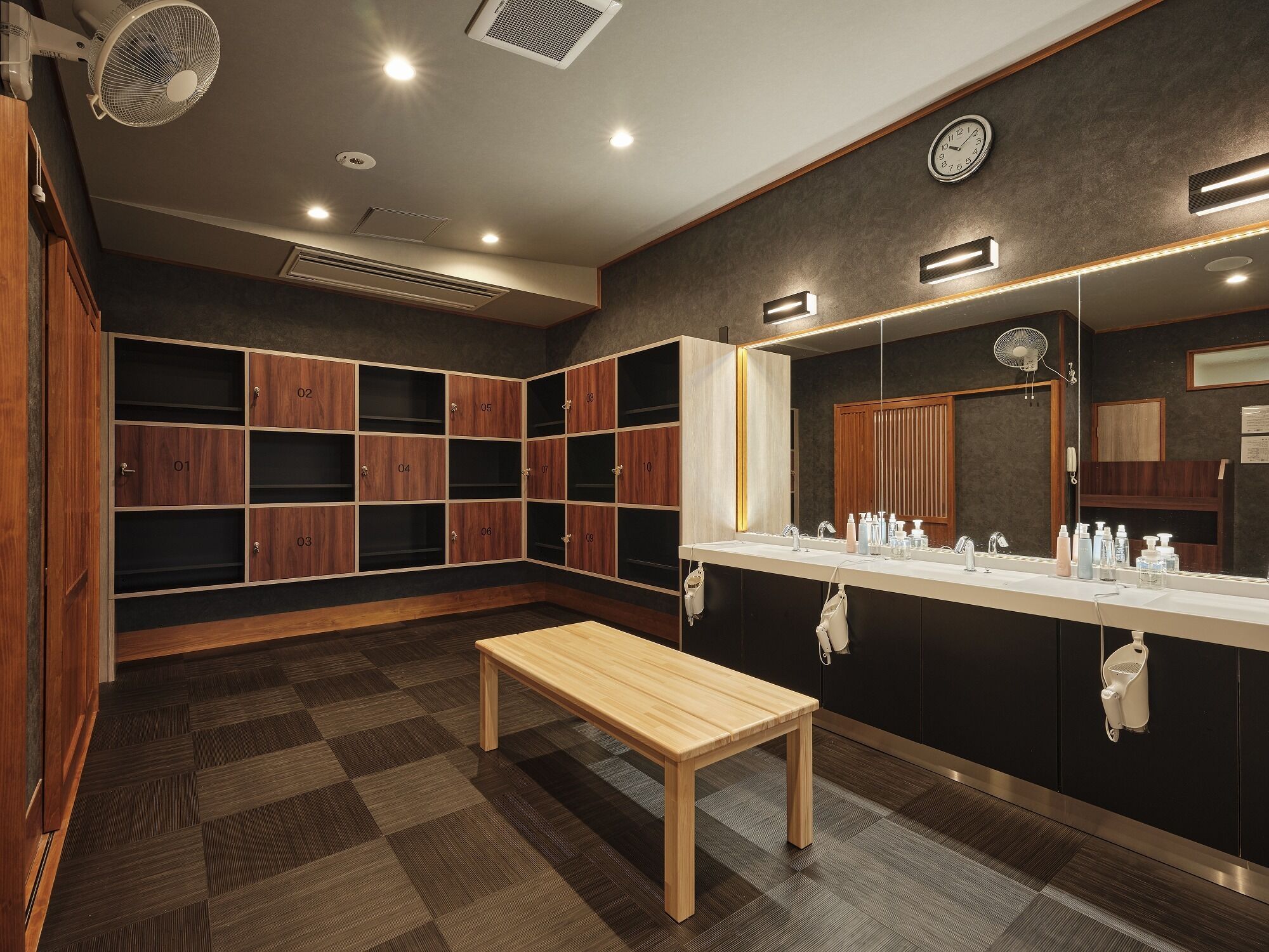 A modern bathroom with a large mirror, wooden lockers, a bench, and a vanity with toiletries.