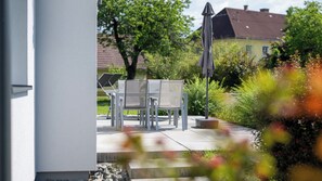 Une terrasse extérieure avec une table et des chaises, une plante en pot et une maison en arrière-plan.