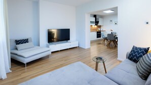 Ein modernes Wohnzimmer mit Flachbildfernseher, einer Couch, einem Couchtisch und einem Essbereich mit Stühlen und Tisch.