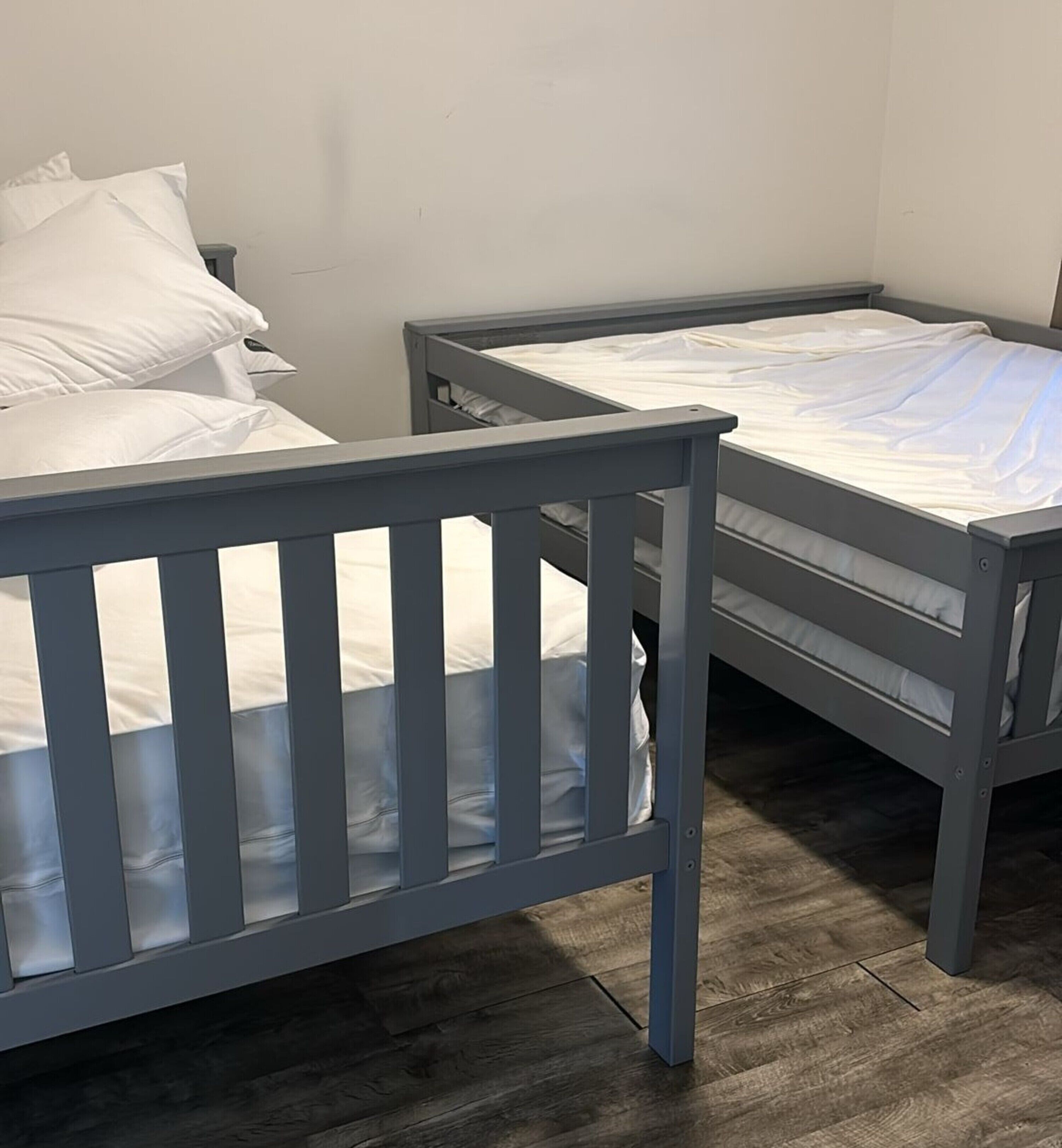 A room with two bunk beds, each with a wooden frame and white bedding.