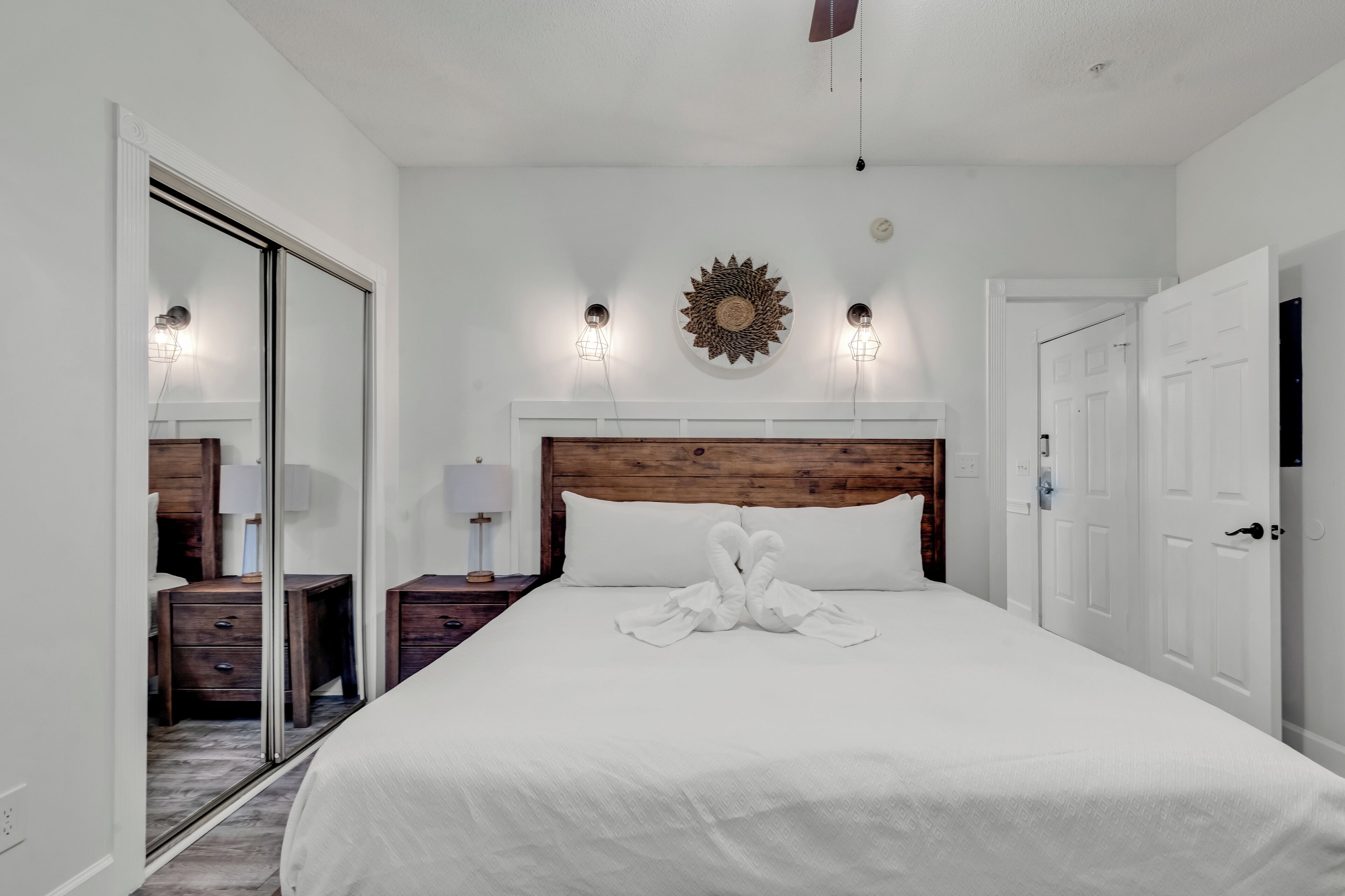 Een slaapkamer met een houten hoofdbord, een groot bed met witte lakens, twee bedlampen en een decoratief object aan de muur.