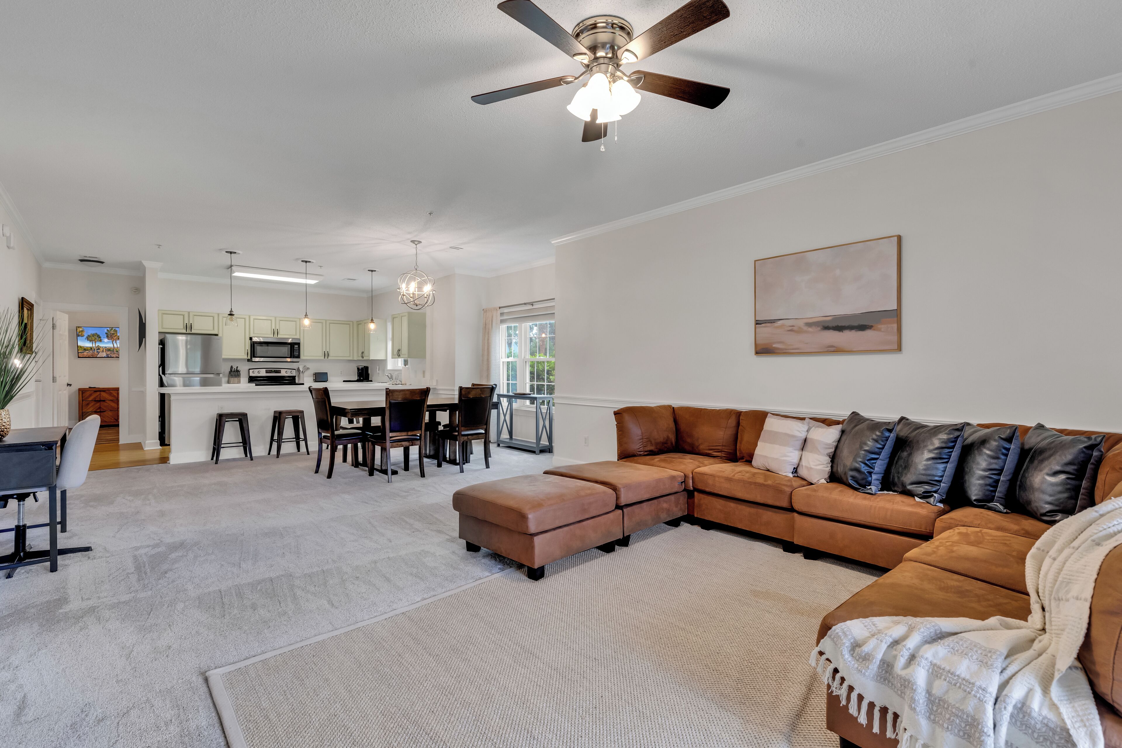 A spacious living room with a large sectional sofa, a dining area with a kitchen in the background, and a ceiling fan.