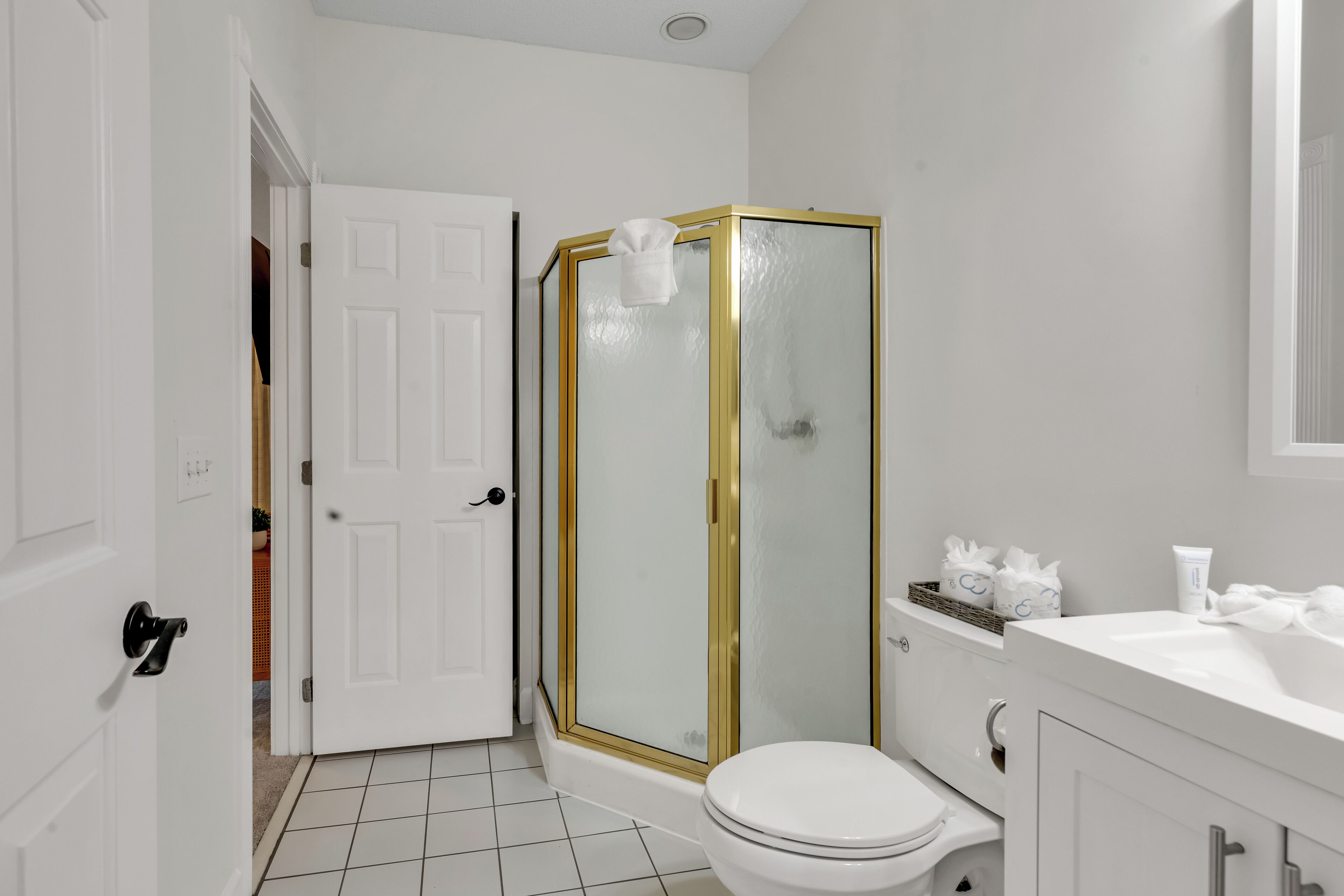 A bathroom with a white toilet, a shower with a gold frame, and a white sink.