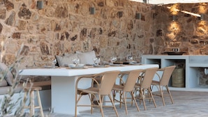 Un muro de piedra con una mesa y sillas, un banco de piedra y una pequeña zona de cocina con una cesta.