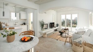 Una cocina moderna con armarios blancos, un comedor con mesa redonda y una sala de estar con sofá y televisor.