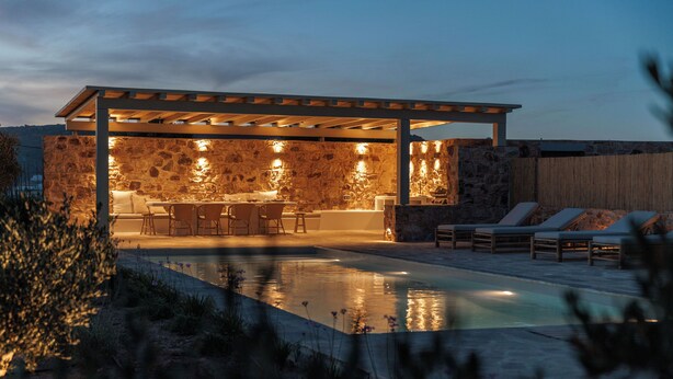 Cocina exterior cubierta con paredes de piedra y una piscina.