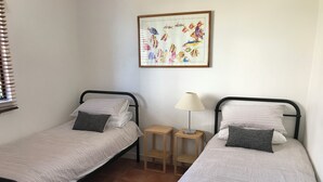 A room with two single beds, each with a pillow and a bedside table. There is a framed picture on the wall above the beds.