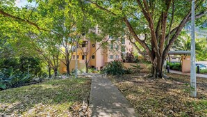 A pathway leading to a building with multiple balconies, surrounded by lush greenery and trees.