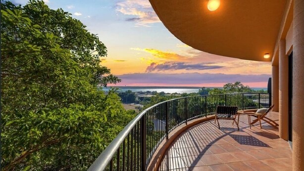 A balcony with a curved railing, a view of the landscape, and a sunset.