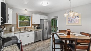 A modern kitchen with white cabinets, stainless steel appliances, and a dining area with a wooden table and chairs. - Charming Family Home in Burnsville (Burnsville)