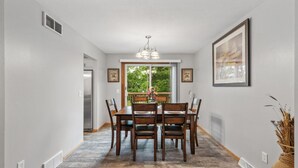 A dining area with a wooden table and chairs, a chandelier, and a view of greenery through a window. - Charming Family Home in Burnsville (Burnsville)