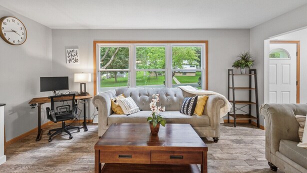A living room with a sofa, coffee table, and a desk with a computer. There is a window with a view of a green landscape. - Charming Family Home in Burnsville (Burnsville)