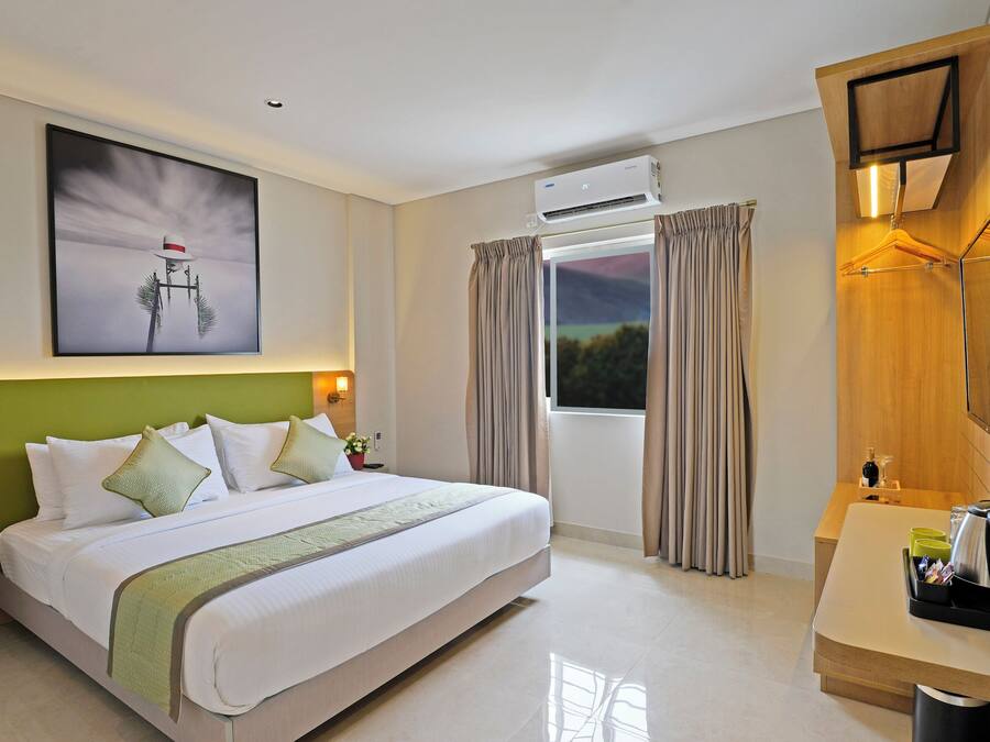 Habitación de hotel con una cama grande, un escritorio con espejo, un equipo de aire acondicionado y un cuadro en la pared.