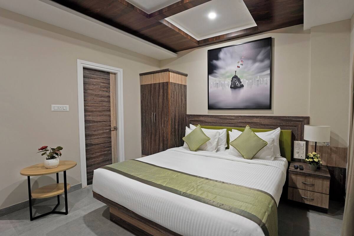 A hotel room with a large bed, a nightstand, a small table with a vase of flowers, and a painting on the wall.