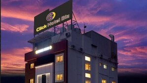 Et hotel med et tydeligt skilt øverst, der siger "Click Hotel Biz". Bygningen har flere etager med vinduer, der er oplyst indefra.