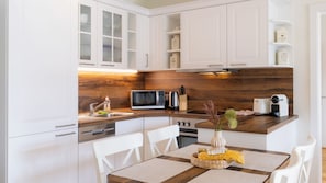 A modern kitchen with white cabinetry, a wooden countertop, a microwave, a coffee maker, and a dining area with a table and chairs.