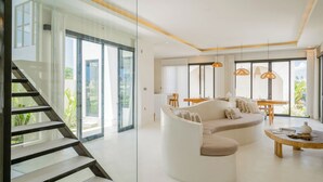 A modern living room with a curved sofa, a wooden coffee table, and a staircase leading to a balcony.