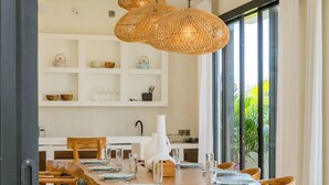 A dining area with a wooden table, wicker chairs, and hanging wicker pendant lights.