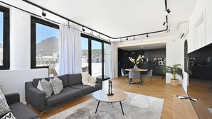 A modern living room with a gray sofa, a coffee table, and a dining area with a table and chairs. - City Centre Rooftop Penthouse with 360° City & Mountain Views! (Cape Town)