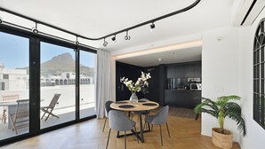 A modern dining area with a round table, grey chairs, and a vase of white flowers. - City Centre Rooftop Penthouse with 360° City & Mountain Views! (Cape Town)