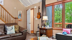 A cozy living room with a brown leather couch, a wooden coffee table with playing cards, a lamp, and a guitar on a stand.