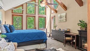 A bedroom with a large bed, a desk, a fireplace, and multiple windows.