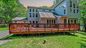 A two-story house with a deck, surrounded by trees.