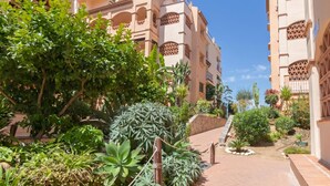Un cortile con un sentiero, circondato da edifici con finestre ad arco e balconi, e diverse piante.
