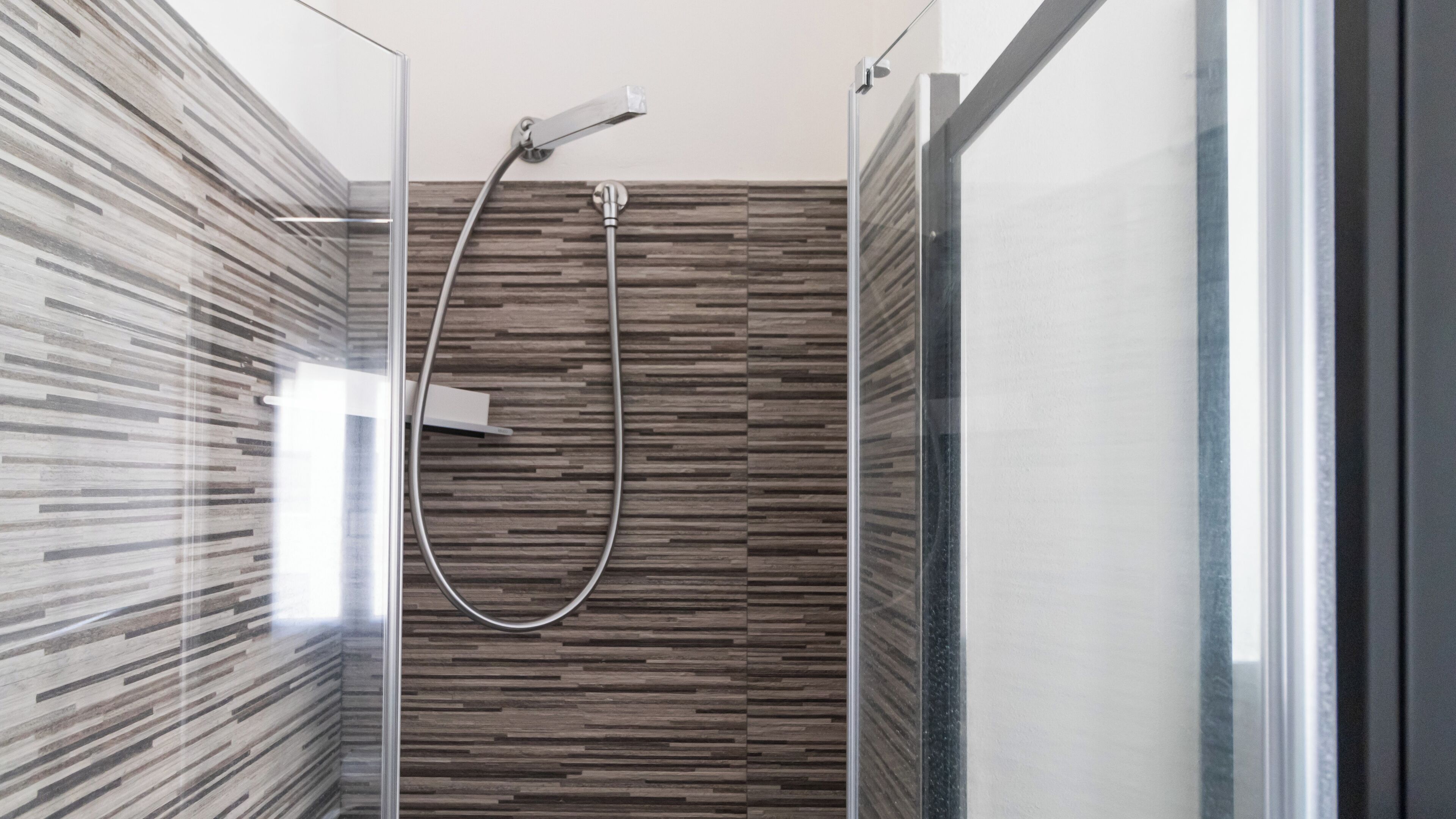 A modern shower with a glass door, a wooden panel wall, and a chrome showerhead.