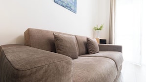 Un canapé marron avec trois coussins, dans une pièce dont le mur est blanc et qui possède une fenêtre.