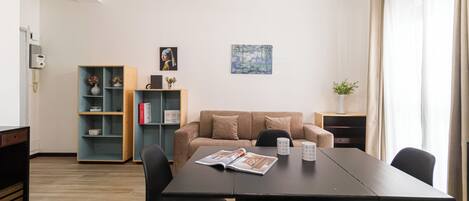 A modern living room with a sofa, a coffee table with magazines, a bookshelf, and a painting on the wall.
