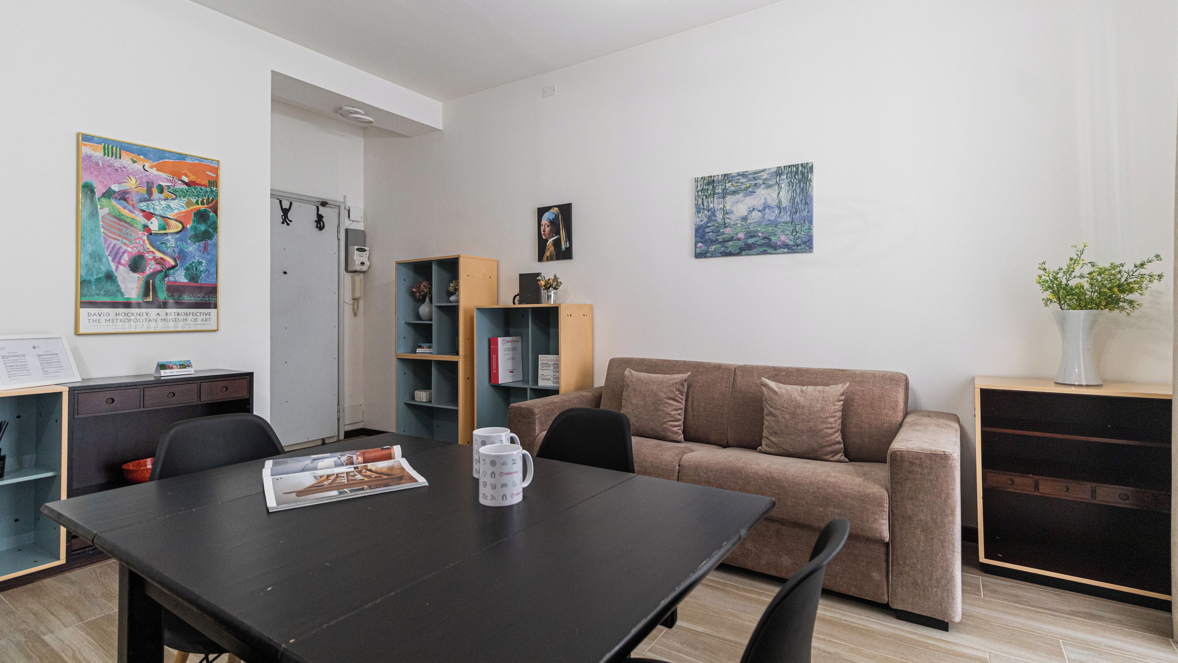 A modern living room with a black dining table, a brown sofa, and a bookshelf.