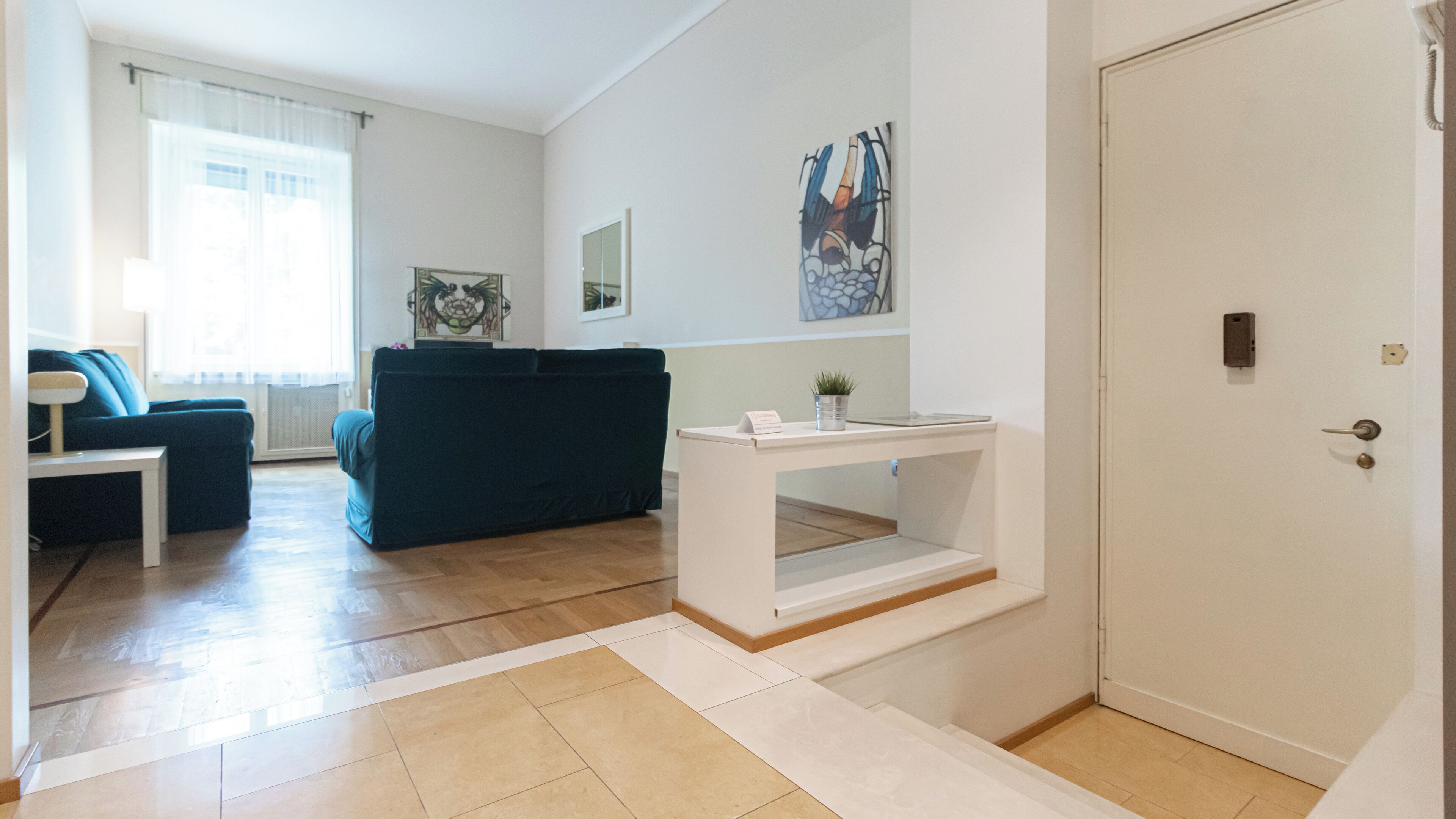 Un salon moderne avec un canapé bleu foncé, une console blanche ornée d’une plante et une porte dotée d’un dispositif de sécurité.