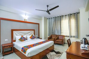 A hotel room with a bed, a chair, a table, a ceiling fan, and curtains. - Fabhotel Corporate Park (New Delhi)