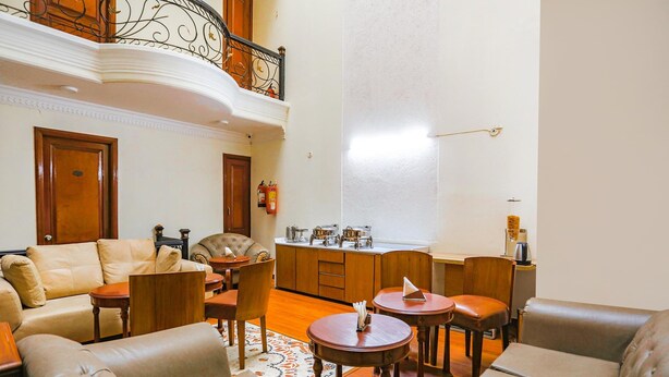 Un vaste salon doté d’un haut plafond, un balcon orné de balustrades en fer forgé et une cuisine avec des meubles en bois et un plan de travail.