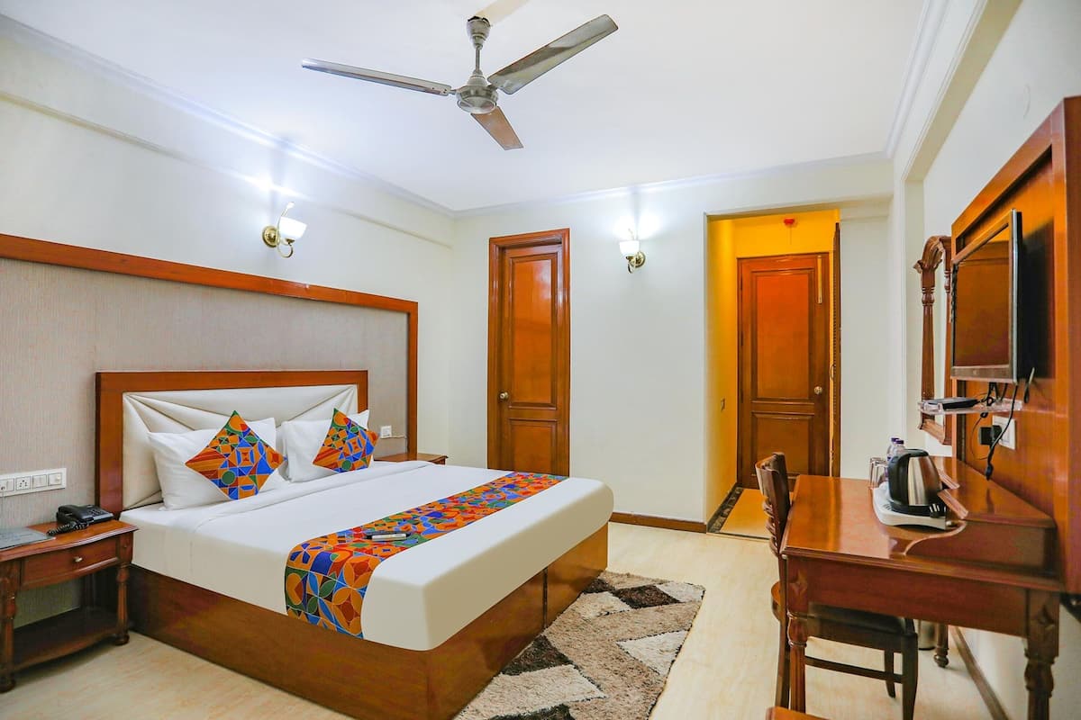 Habitación de hotel con cama, escritorio, silla, ventilador de techo y una puerta.