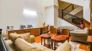 Un salon comprenant un canapé, une table basse et des fauteuils, un coin cuisine avec un comptoir et des placards, et un escalier doté d’une rampe en fer forgé.