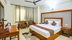 Une chambre d’hôtel avec un grand lit, un bureau, deux chaises, un ventilateur de plafond et une fenêtre avec des rideaux.