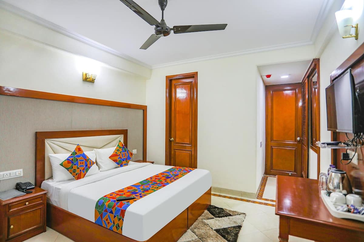 Una habitación de hotel con una cama, una mesita de noche, un escritorio con una silla, un ventilador de techo y un televisor.