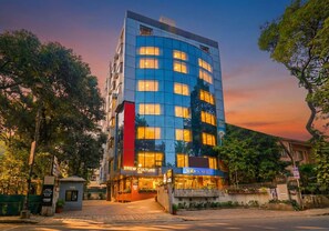 A modern hotel with a glass facade, multiple floors, and a well-lit entrance. - Oriva Deccan 8 (Pune)