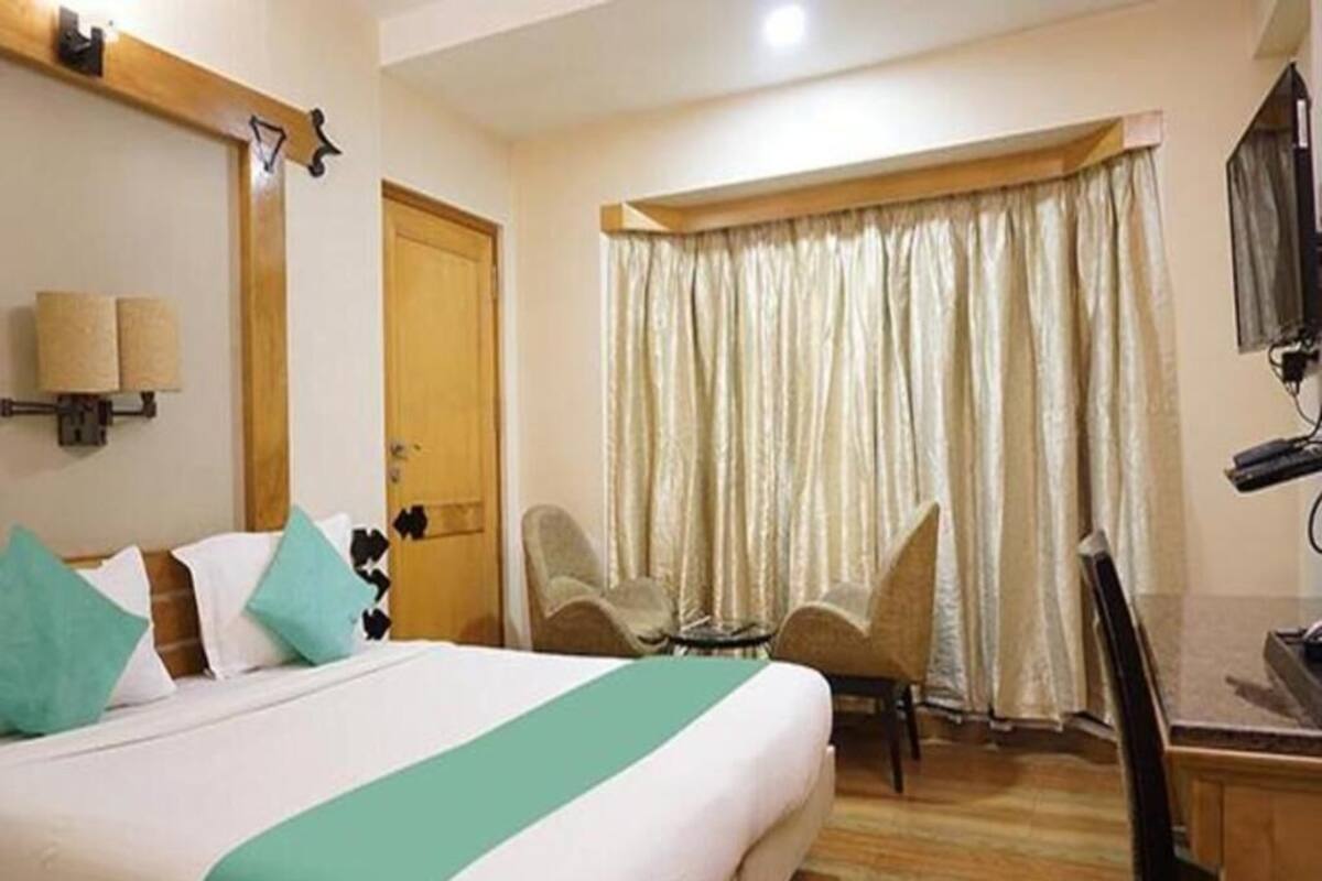 A hotel room with a bed, a desk, a chair, a television, and a window with curtains.