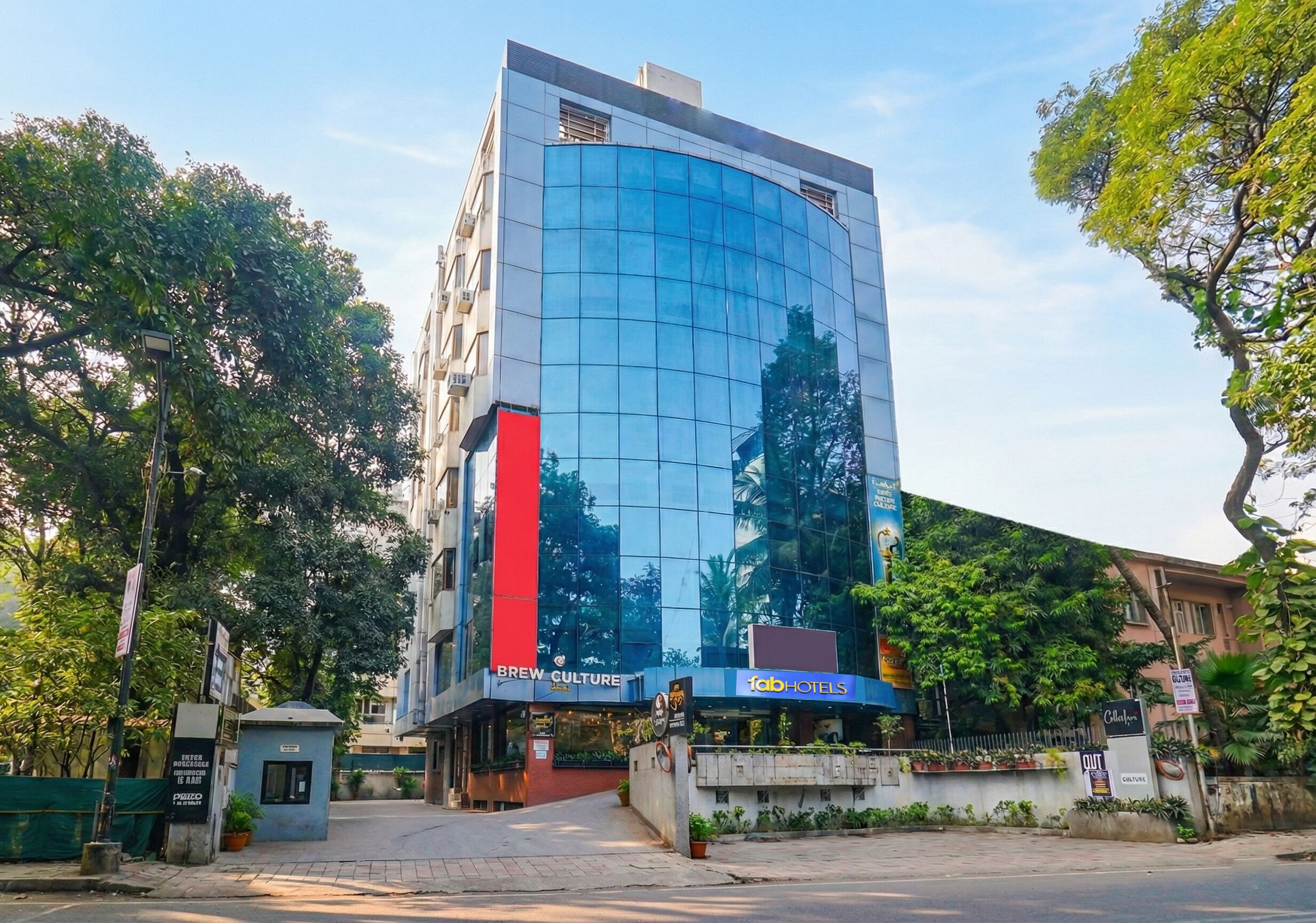 A modern hotel with a curved glass facade, a prominent red vertical feature, and signage for 'Brew Culture' and 'Fab Hotels'.